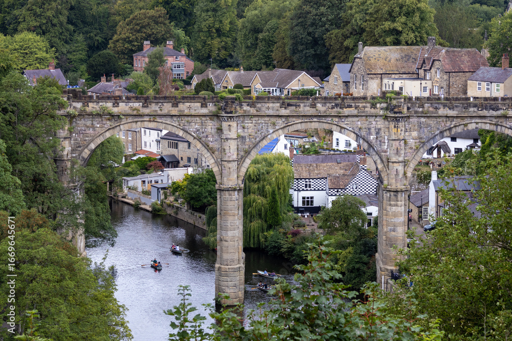Fototapeta premium Scenic view of the historic stone viaduct crossing the River Nidd in Knaresborough, North Yorkshire, with houses and trees along the riverside