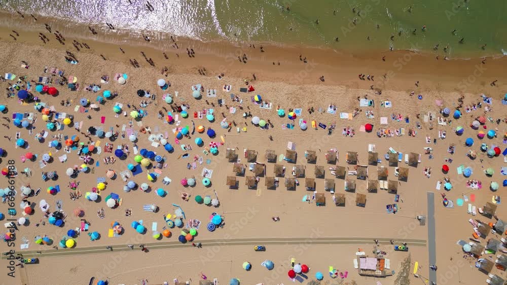 View from above and from the side, the beautiful Guincho beach full of people with parasols adding color to the beach and waves breaking on the seashore,Cascais,Portugal