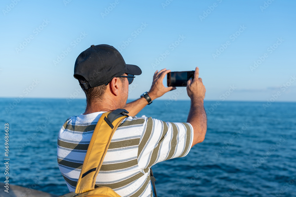 Obraz premium Mature latin american man taking photos of the mediterranean sea with smartphone in Sitges, Barcelona