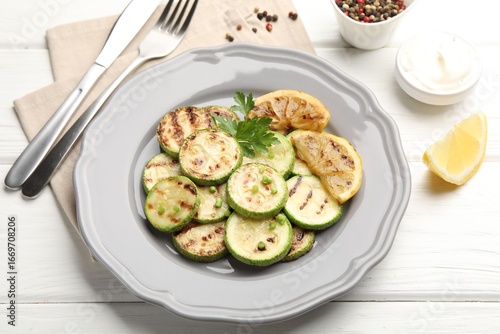Delicious fried courgette slices with lemon and parsley served on white wooden table, closeup