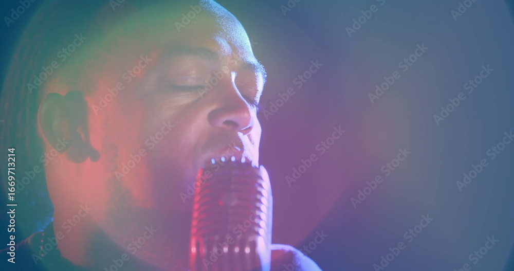 Fototapeta premium Singing male singer wearing dark shirt, holding retro microphone on stage with colored spotlights