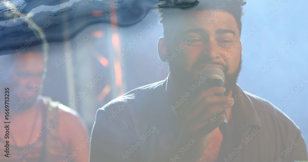 Fototapeta premium Singing bearded lead singer holding microphone on dimly lit stage, with foggy haze and metal truss