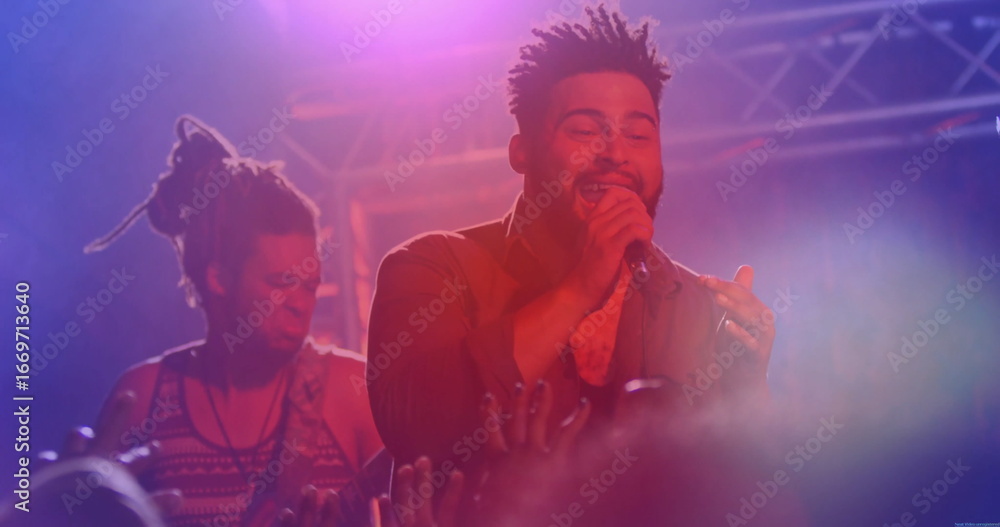 Fototapeta premium Performing mid adult singer gripping microphone, singing on concert stage, with guitar and fog haze