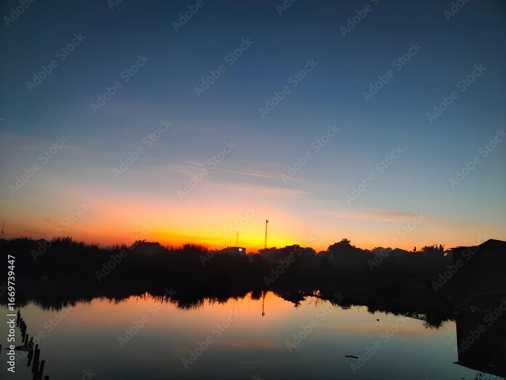 Fototapeta premium Beautiful sunrise over a calm river with colorful sky reflecting on the water, creating a peaceful and serene landscape.