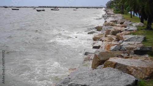 Sea waves crashing against rock with group of small boat mooring and jetty background