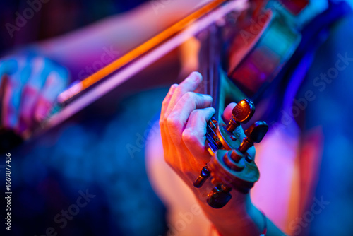 Close-up of woman hands playing violin under colorful stage lights
