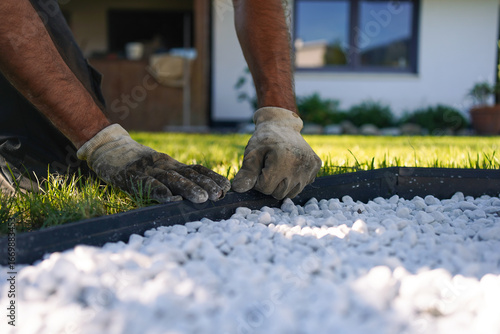 Garden worker's hands placing a Anthracite Metal Edge around a White Pebble Garden Bed