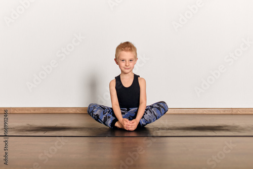 Quadro su tela Young blond boy performs yoga in serene studio, seated cross-legged on mat
