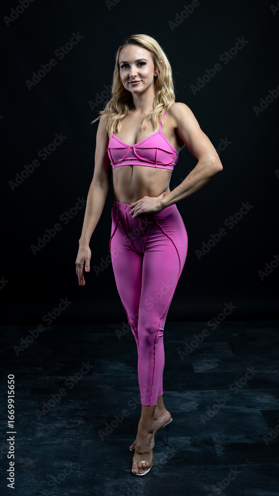 Fototapeta premium Athletic woman wearing pink sportswear showing her sculpted abs while posing on a black background 