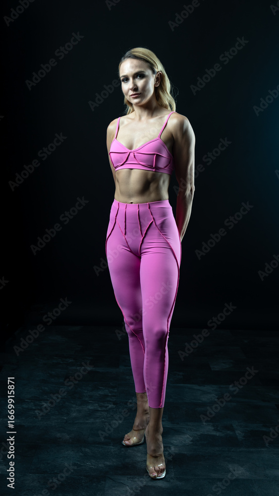 Fototapeta premium Athletic woman wearing pink sportswear showing her sculpted abs while posing on a black background 