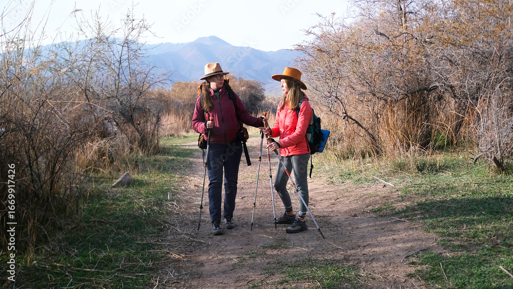Fototapeta premium Two female hikers stood on a dirt path to discuss the further route. The sisters travel together. Travelers are relaxing after a long day at sea