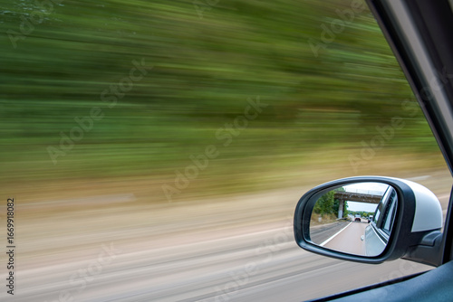 Traveling by car picture with motion blur from the window of a moving car. Focus on the wing mirror. Driving at speed. Automobile and transportation image.