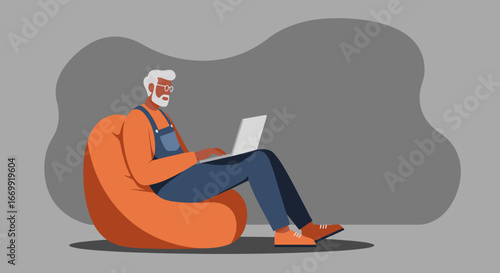 Modern senior man in overalls comfortably using a laptop on a beanbag chair, embracing technology and remote work at home.