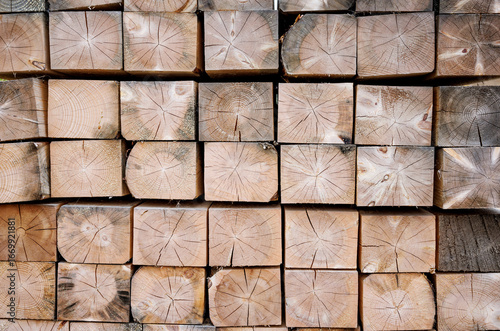 A folded bar in a stack. The end part is made of treated wooden beams. Background with a wood texture. Industrial texture of lumber. A close-up background image of a stack of wooden beams.