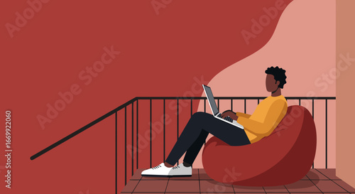 African American man working on a laptop while relaxing on a bean bag chair on a modern balcony. Remote work, freelancing, and digital lifestyle.
