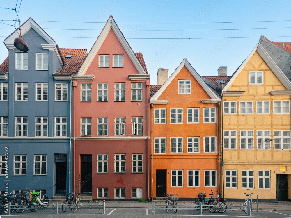 Fototapeta premium Colorful historic townhouses with steep roofs line Landemærket street in Copenhagen, Denmark, with bicycles parked along the sidewalk under a clear blue sky.