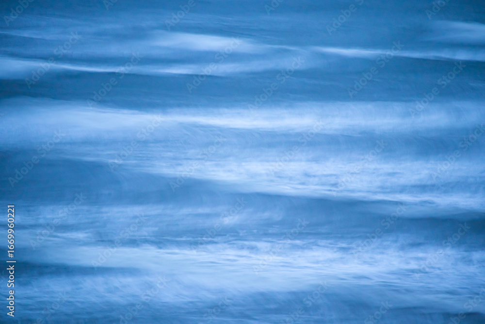 Fototapeta premium Long exposure creating an abstract impression of ocean waves with flowing streaks of soft blue and white patterns