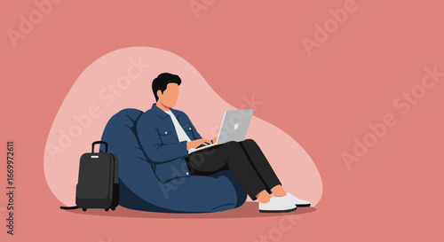 Young man working remotely on laptop from a comfortable bean bag chair with luggage. Ideal for digital nomad, remote work, and modern travel concepts.