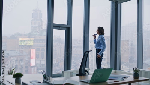 Foto Business manager recording voicemail at smartphone standing by office window
