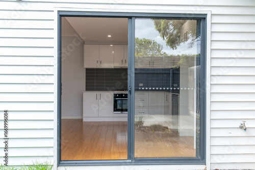 Sliding glass door entry to kitchen space with white cabinets, wooden floor and grey backsplash, modern minimalist interior design