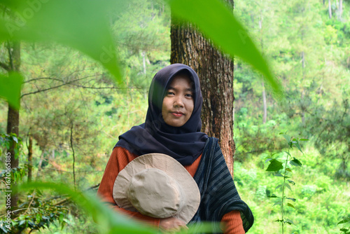 Young Asian Muslim woman hiking and camping in autumn forest, smiling at camera wearing Javanese ethnic clothes