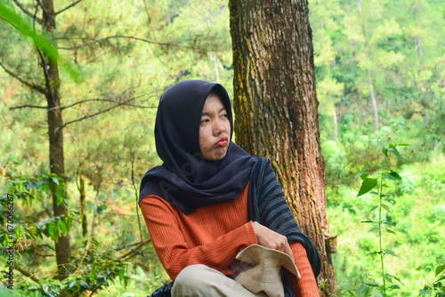 Young Asian Muslim woman hiking and camping in autumn forest, smiling at camera wearing Javanese ethnic clothes