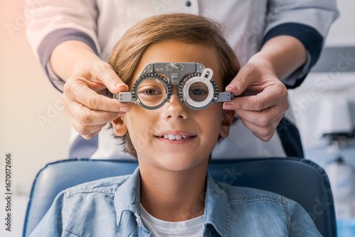 Smiling child boy in glasses checks eye vision at pediatric ophthalmologist. Small patient undergoing eye sight correction, choosing lenses frame for glasses in clinic hospital