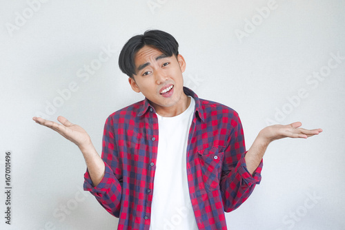 Young man shrugs shoulders, expressing uncertainty or indifference against a plain background.