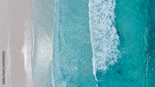 Aerial of crystal blue waves crashing onto perfect white sand