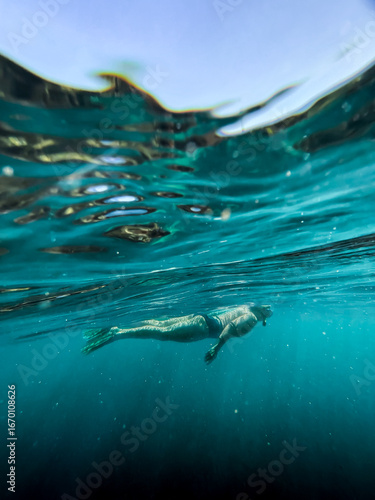 Underwater of female snorkelling in ocean afloat at surface looking down