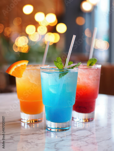 Three colorful cocktails with straws and mint on a table with bokeh lights in the background