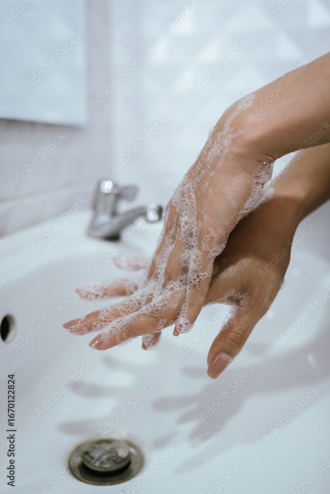 Fototapeta premium A woman washes hands with soap and water in a bathroom sink, creating bubbles and foam for hygiene, health, and cleanliness.