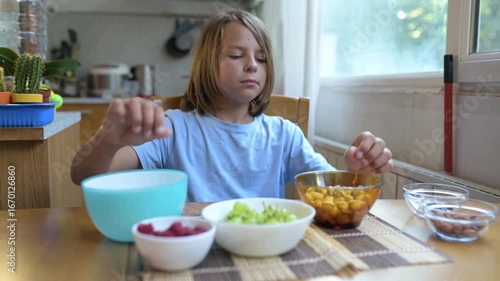 Young child eating pistachios at home dining table. Casual and cozy kitchen setting with natural light, relaxed mood, and healthy nut snack