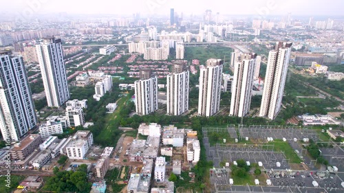 Aerial drone shot slow orbit around sky scraper multi story building with power distribution center small houses and gurgaon cityscape stretching in distance
