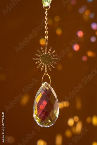 Glass suncatcher with metal golden chains, shining in sunlight and reflecting the rainbow on a yellow background