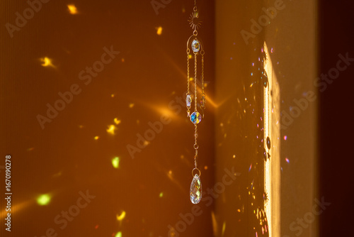 Glass suncatcher with metal golden chains, shining in sunlight and reflecting the rainbow on a yellow background