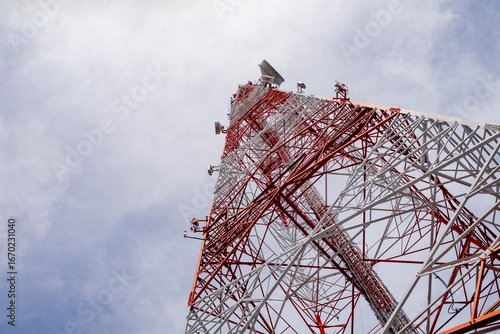 Low-angle view of a red and white telecommunications tower structure against a bright sky, highlighting modern engineering, symmetry, and industrial design.