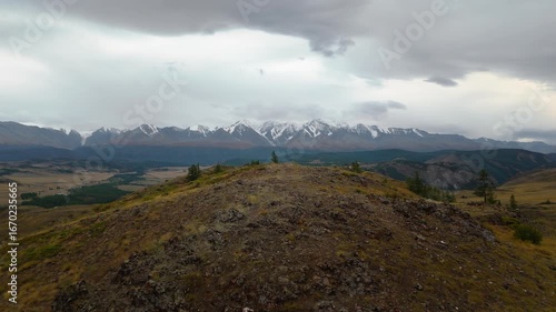 Scenic aerial panorama of Mount Belukha in Altai Republic. Snowy peaks, cloudy sky, and vast valleys create a dramatic wilderness landscape for tourism and environment themes.