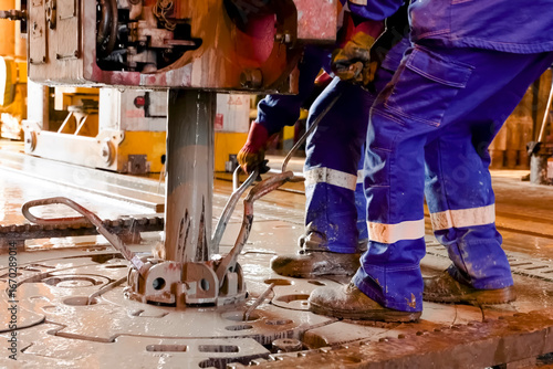 Driller's assistants near the drilling table on oil drilling platform soiled the overalls with drilling fluid.