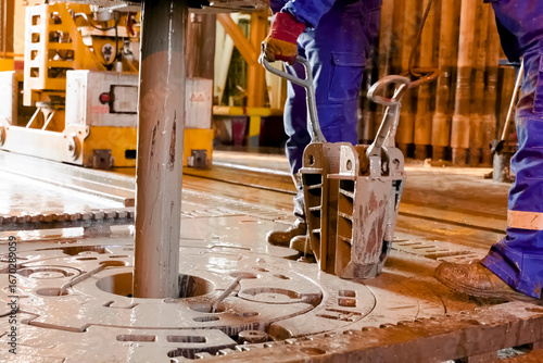 Driller's assistants near the drilling table on oil drilling platform soiled the overalls with drilling fluid.
