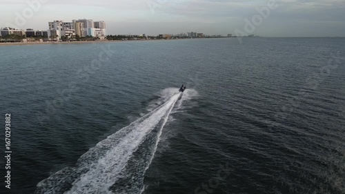 A view from above of a person on a jet-ski out in the ocean with the coastline in the background