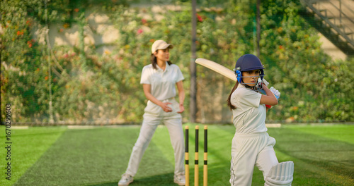 Indian gen z young adult sports woman girl standing at outdoor match play ground wear gloves white uniform and protective helmet Asian athlete cricket player female lady hold bat do practice day time
