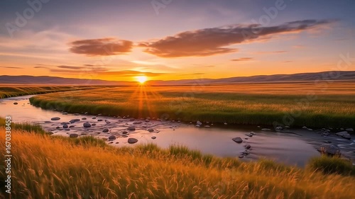Sun sets on a field of grass, shining onto a winding rocky river in a quiet landscape