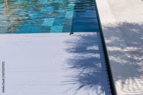Fotografie Zoom sur le fond d’une piscine en carrelage avec des carreaux multicolores formant un jeu de textures et de nuances avec une bâche électrique qui se referme