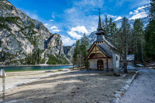 Scenic Lago di Braies, Italy, featuring its quaint chapel, traditional wooden rowboats, and peaceful shoreline backed by dense trees. A beautiful Dolomite lake view.