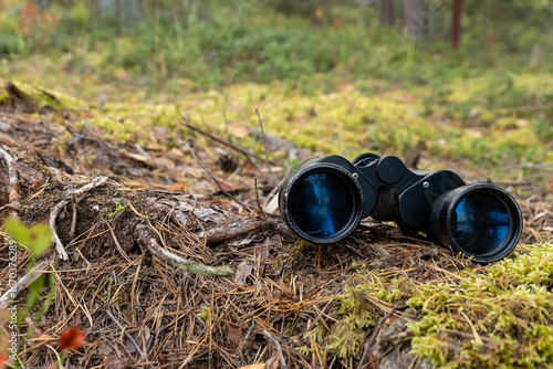 Binoculars resting on mossy forest floor with dry leaves