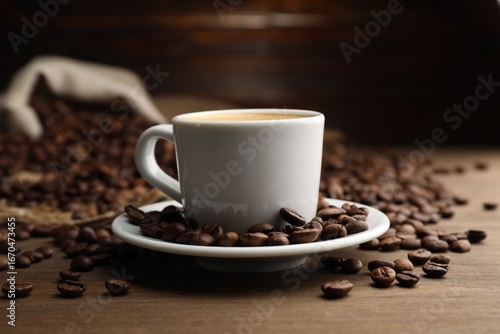 Aromatic coffee in cup and beans on wooden table, closeup