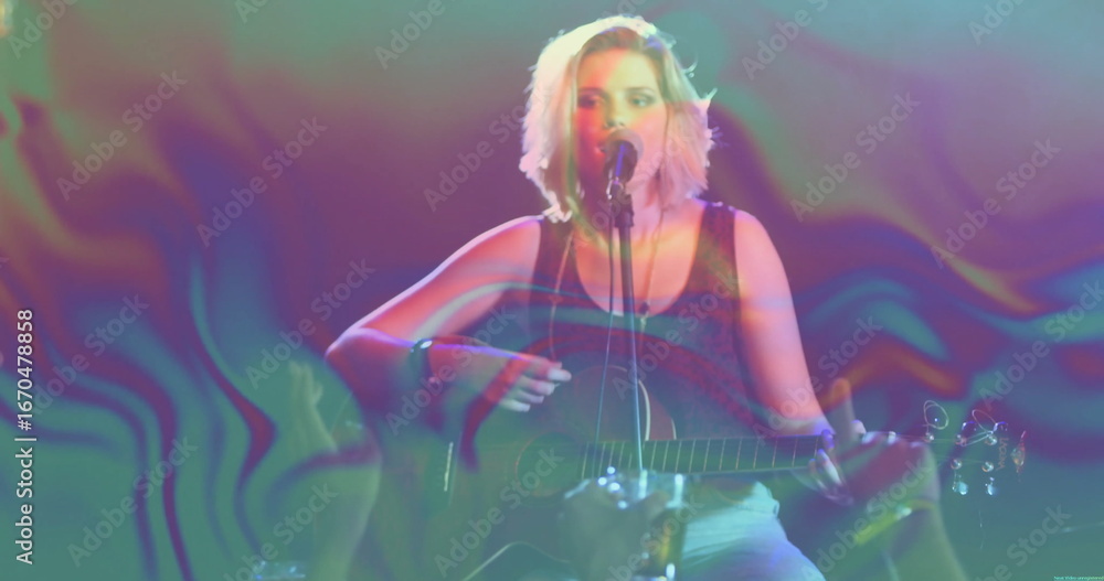 Fototapeta premium Strumming teen musician singing on stage, with acoustic guitar, microphone stand and stage lights