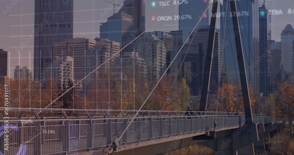 Fototapeta premium Walking pair in fall jackets crossing pedestrian suspension bridge among autumn trees, data overlay