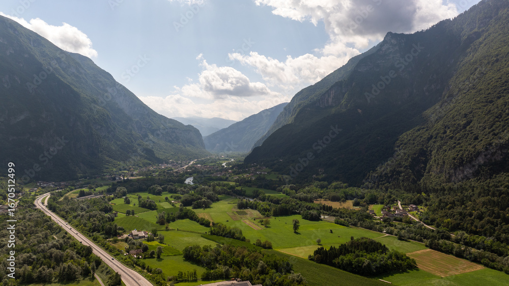 Fototapeta premium Aerial view of the Valsugana highway crossing the green valley surrounded by mountains in Grigno, Trentino, Italy
